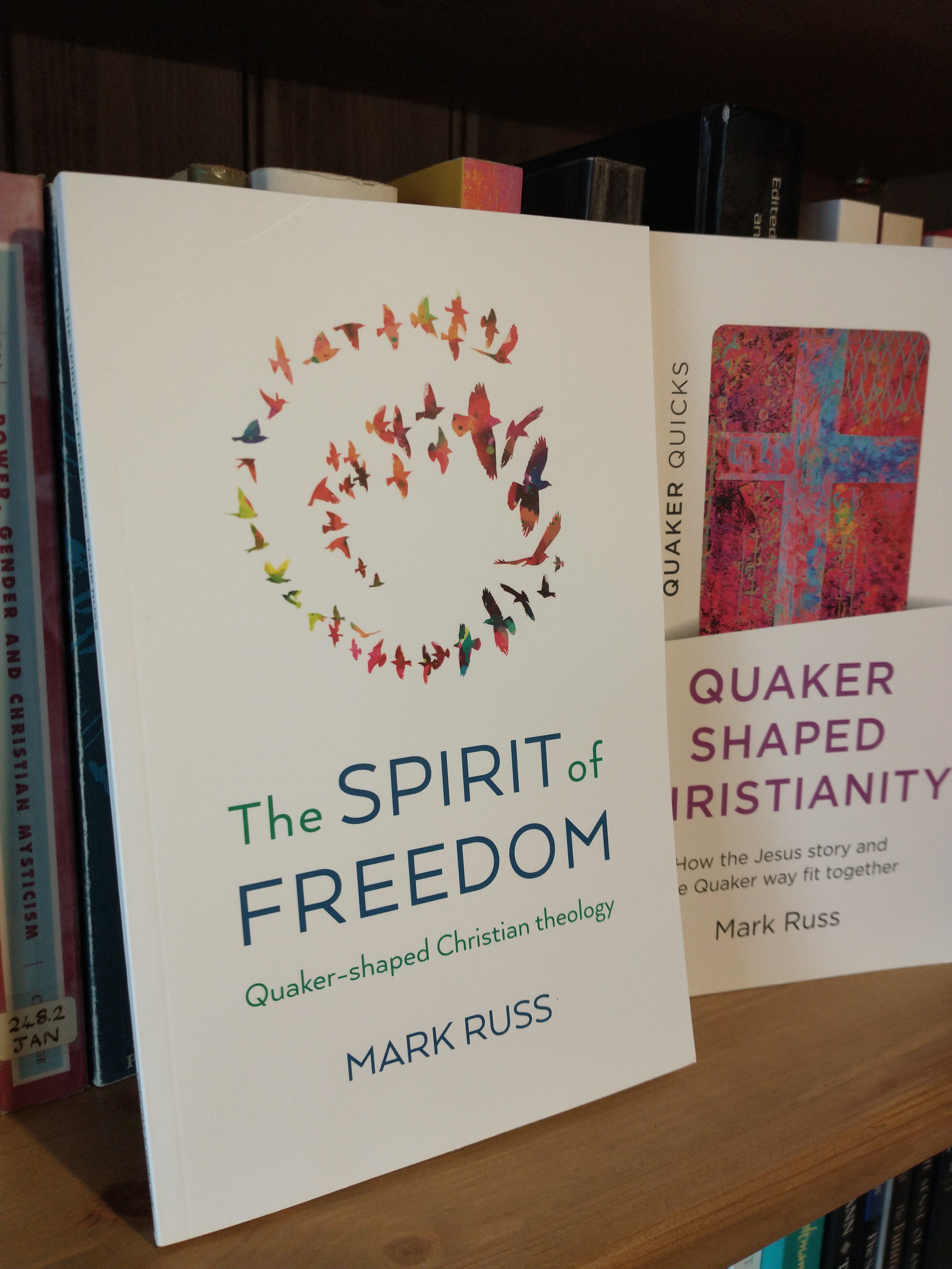 A copy of 'The Spirit of Freedom' on a bookshelf, next to the book 'Quaker Shaped Christianity.'